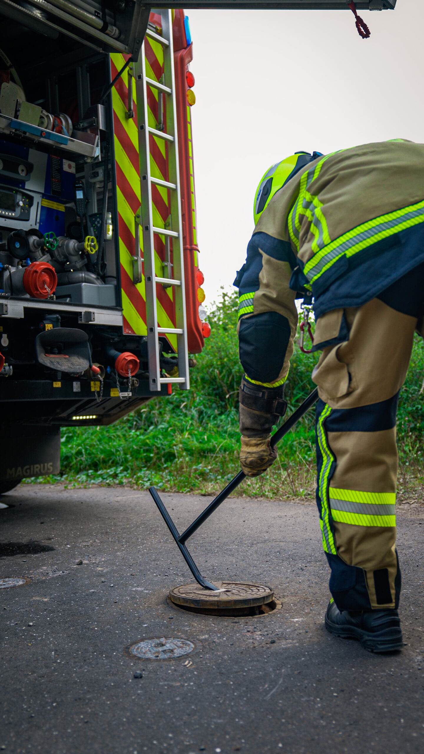 Feuerwehrmann in Einsatzkleidung öffnet mit dem Hydrantenschlüssel einen Unterflurhydranten neben einem Löschfahrzeug